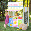 Two girls playing with Kids Lemonade Stand outdoors in backyard with chalkboard menu panel and service window