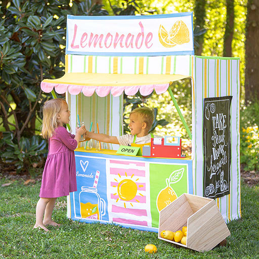Two girls playing with Kids Lemonade Stand outdoors in backyard with chalkboard menu panel and service window