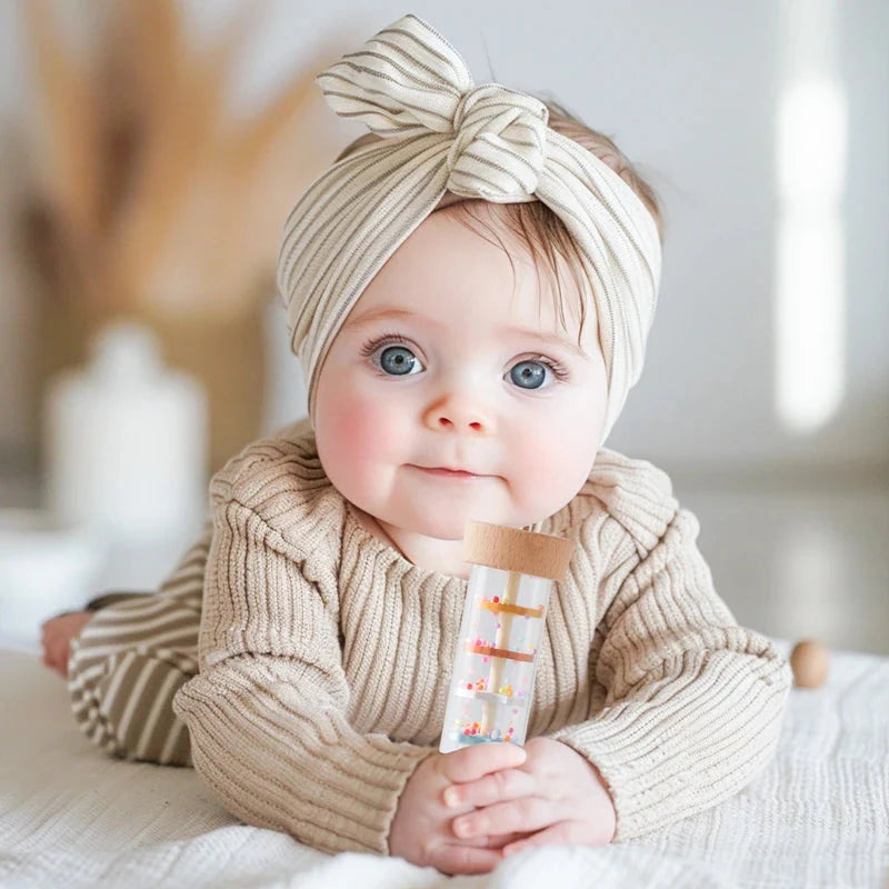 Smiling baby holding Montessori rain stick rattle toy showing easy-to-grasp size for small hands